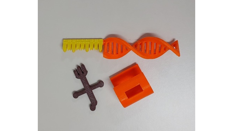 A imagem apresenta o recurso didático denominado Material Genético, confeccionadas em plástico, por impressão 3D, e é composto por 4 peças, sendo uma delas que representa o DNA, o ribossomo, o RNA mensageiro e o RNA transportador.
