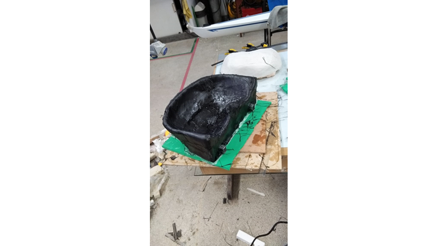 A imagem apresenta a foto de um assento, feito em estrutura de alumínio e fibra de carbono, de um barco a remo.