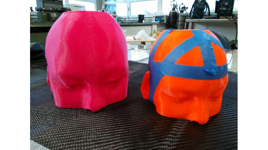 A imagem apresenta a foto de dois modelos de plástico de cabeças dispostos uma ao lado do outro e sobre uma mesa. Um deles possui cor laranja e o outro a cor rosa.