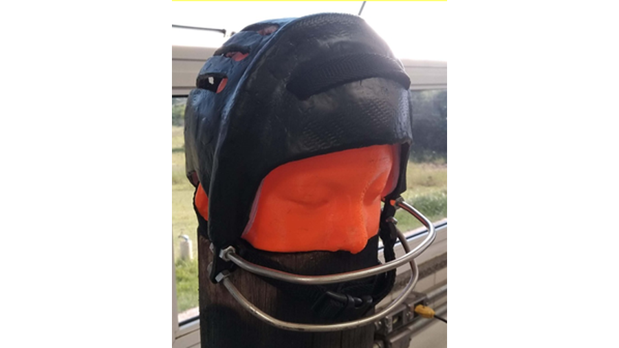 A imagem apresenta a foto de um capacete preto, confeccionado em fibra de carbono, posicionado em uma cabeça de plástico na cor laranja.